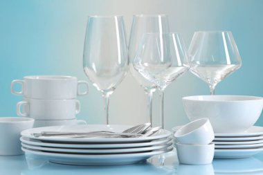 Açık mavi masada bir sürü temiz bulaşık takımı, çatal bıçak takımı ve bardak var.