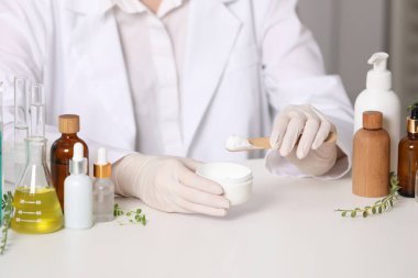 Beyaz masada kavanoz testi kozmetik ürünü olan bir cildiyeci, yakın plan.