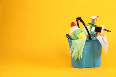 Sarı arkaplanda kovadaki farklı temizlik ürünleri, metin için yer