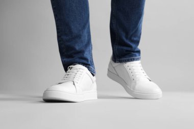 Gri arka planda şık beyaz ayakkabılar giyen adam, yakın plan.