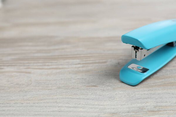One light blue stapler on wooden table, closeup. Space for text