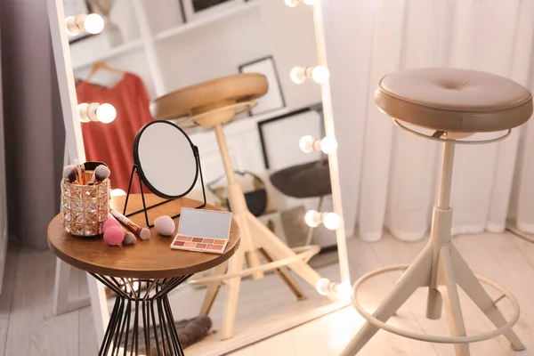 Makeup room. Stylish mirror with light bulbs, beauty products on wooden table and chair indoors