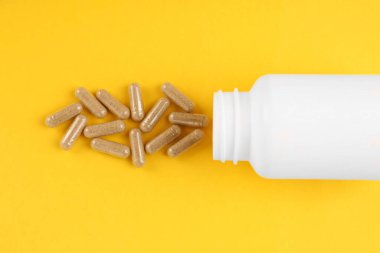 Sarı arka planda beyaz ilaç şişesi ve vitamin kapsülleri.