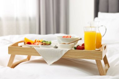 Yatakta servis edilen lezzetli kahvaltı. Yulaf ezmesi, meyve suyu, meyve, badem ve bal ahşap tepside.