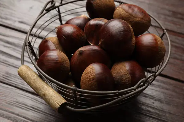 stock image Sweet fresh edible chestnuts in metal basket on wooden table, closeup