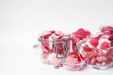 Cam kavanozlarda farklı lezzetli pembe şekerler ve beyaz arka planda kaseler, metin için yer.