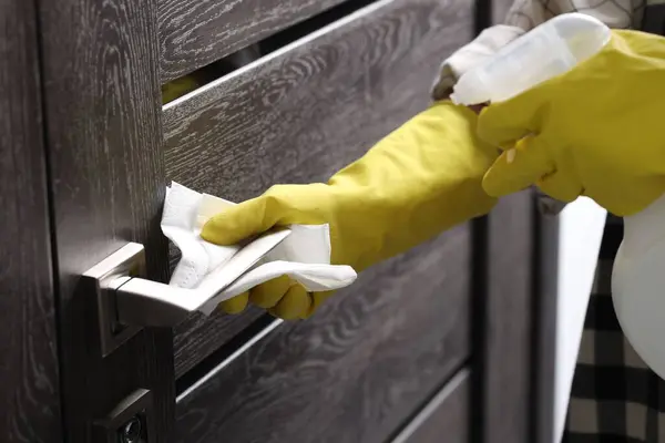 Woman cleaning door handle with detergent and paper towel, closeup