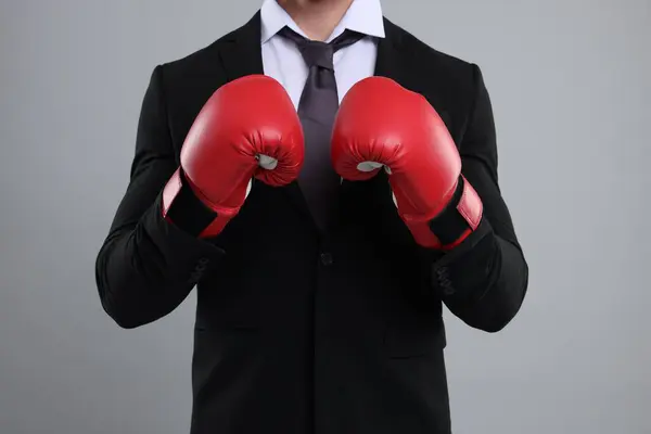Businessman in suit wearing boxing gloves on grey background, closeup