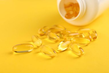 Sarı arka planda vitamin kapsülleri ve tıbbi şişe, yakın plan.