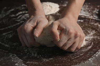 Ekmek yapıyorum. Ahşap masada hamur yoğuran kadın, yakın plan.