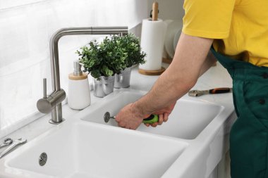Üniformalı tesisatçı mutfakta lavabo tamir ediyor, yakın plan.