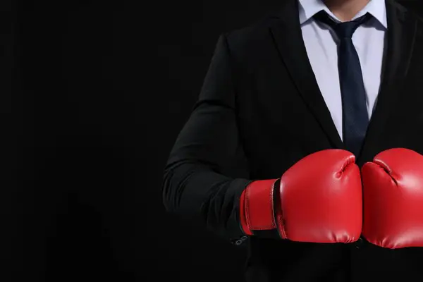 Businessman in suit wearing boxing gloves on black background, closeup. Space for text