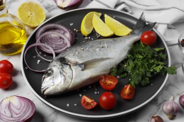 Taze dorado balığı ve malzemeler beyaz mermer masada.