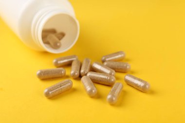 Sarı arka planda vitamin kapsülleri ve tıbbi şişe, yakın plan.