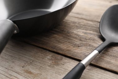 Black metal wok ve spatula ahşap masada, yakın plan.