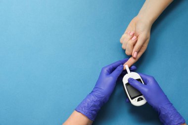 Diyabet. Doktor, mavi arka planda glukometreyle hastanın kan şekerini ölçüyor. Metin için boşluk