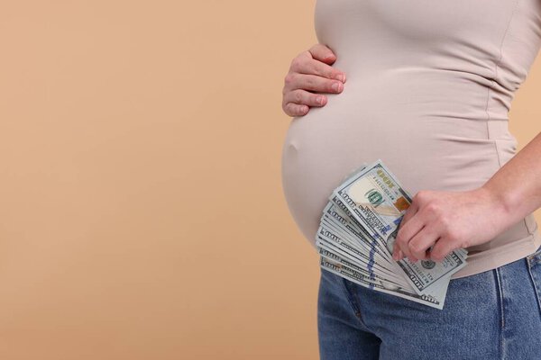 Surrogate mother. Pregnant woman with dollar banknotes on beige background, closeup. Space for text