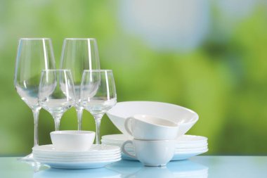 Açık mavi masada bulanık yeşil arka planda bir sürü temiz bulaşık takımı ve gözlük var. Metin için boşluk