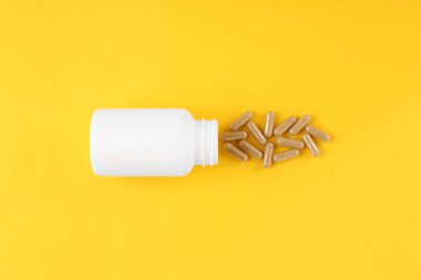 Sarı arka planda beyaz ilaç şişesi ve vitamin kapsülleri.