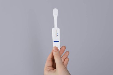 Açık gri arkaplan üzerinde tek kullanımlık ekspres test tutan kadın, yakın plan