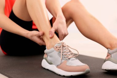 Kadın bacak ağrısından muzdarip. Kapalı alanda paspas üzerinde, yakın plan.