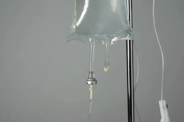 IV infusion set on pole against grey background, closeup. Space for text