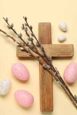 Ahşap haç, boyanmış Paskalya yumurtaları ve bej arka planda söğüt dalları, düz uzanmış