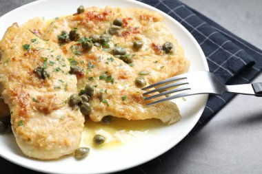 Gri masada servis edilen bitkilerle birlikte lezzetli tavuk piccata, yakın plan.