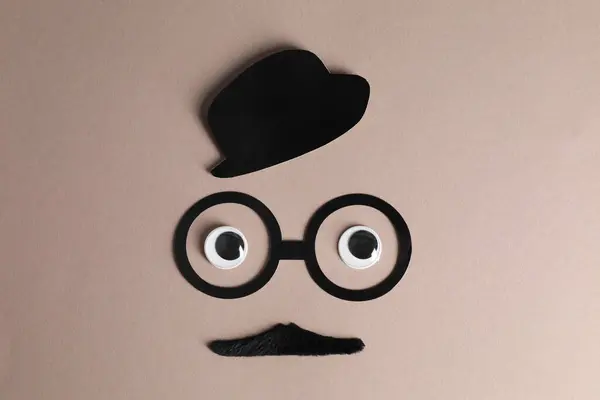 Man\'s face made of fake mustache, paper hat and glasses on grey background, top view