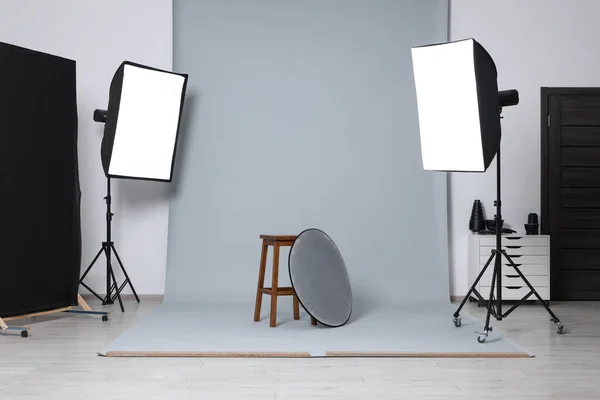 Stool with light reflector surrounded by professional lighting equipment in photo studio