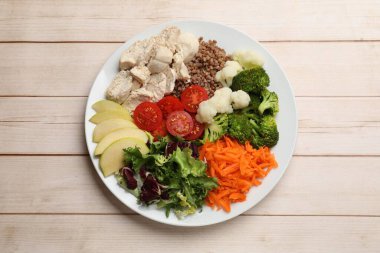 Dengeli beslenme ve sağlıklı yiyecekler. Tabakta farklı lezzetli ürünler var. Hafif ahşap masa, üst manzara.