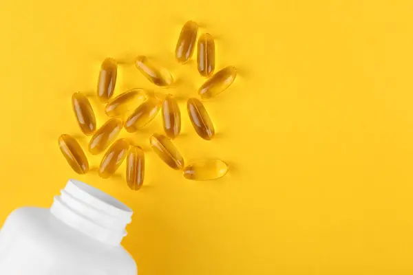 White medical bottle and vitamin capsules on yellow background, top view. Space for text