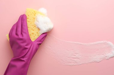 Lastik eldivenli temizleyici süngeri pembe arka planda tutuyor..