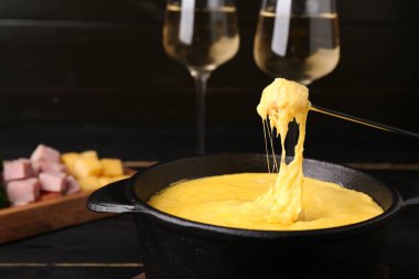 Jambonu fondü kabına daldırmak, erimiş peyniri siyah ahşap masaya koymak, yakın plan.