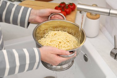 Lavabonun üstünde makarnayı durulayan kadın, yakın plan.