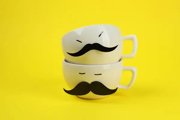Men\'s faces made of cups, fake mustaches on yellow background