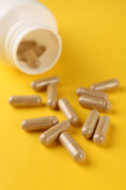 Sarı arka planda vitamin kapsülleri ve tıbbi şişe, yakın plan.