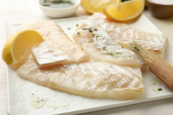 Fresh raw cod fillets with spices, lemon and brush on white table, closeup
