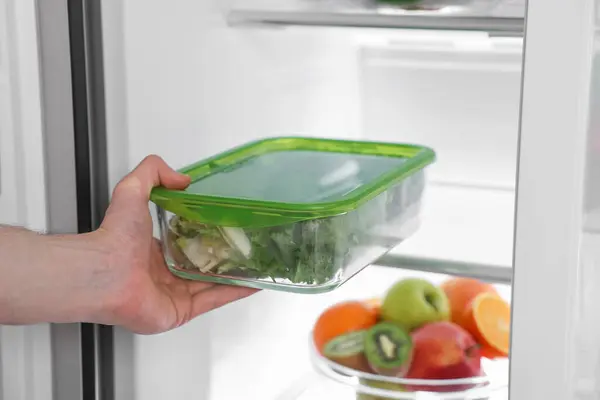 Man putting container with vegetables into refrigerator, closeup