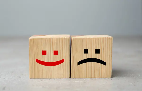 Wooden cubes with happy and sad faces on grey table