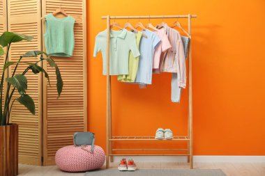 Farklı şık kadın kıyafetleri, ayakkabıları, çantaları ve yeşil çiçekleri turuncu duvarın yanına yerleştirin.