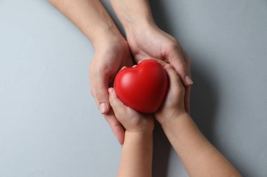 Anne ve çocuğunun elinde gri arka planda kırmızı dekoratif bir kalp var.