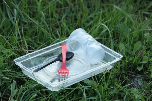 Used plastic tableware on grass outdoors. Environmental pollution concept
