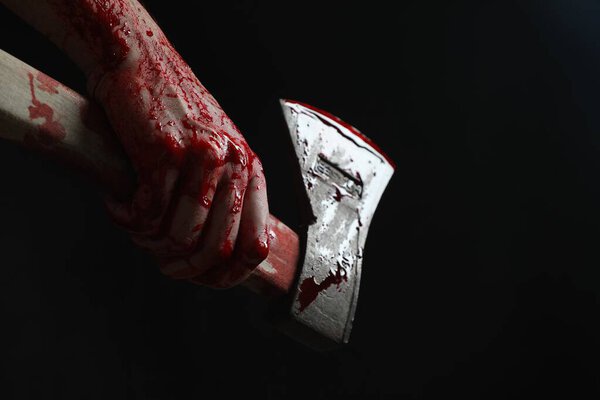 Man holding bloody axe on black background, closeup. Space for text