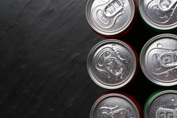 Energy drink in wet cans on black textured background, top view. Space for text