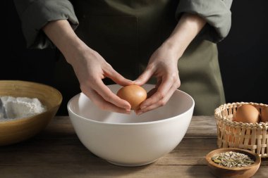 Ekmek yapıyorum. Koyu arka plandaki ahşap masada hamura yumurta ekleyen kadın, yakın plan.