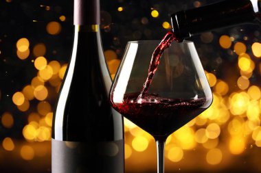 Kırmızı şarabı bardağa ve şişeye doldurup karanlık arka planda bulanık ışıklarla, yakın plan. Bokeh etkisi