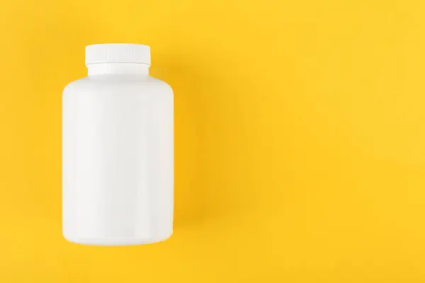 One white medical bottle on yellow background, top view. Space for text