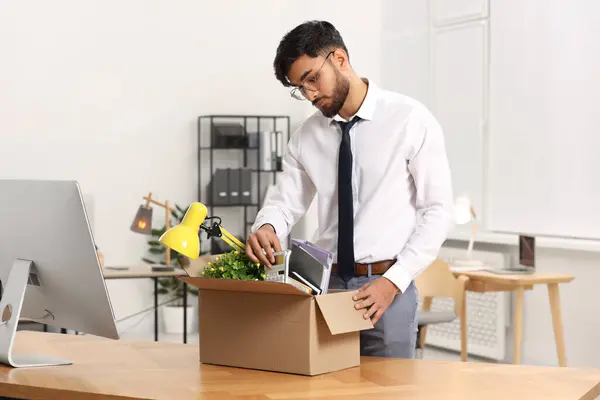 Unemployment problem. Frustrated man with box of personal belongings at table in office
