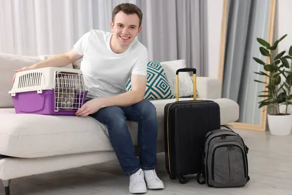Travel with pet. Man near carrier with cat on sofa at home